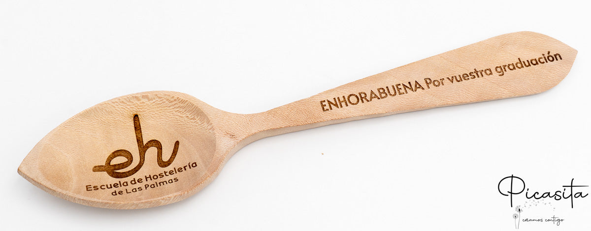Cuchara de madera con dedicatoria de graduación y logotipo institucional en tonos marrones oscuros.