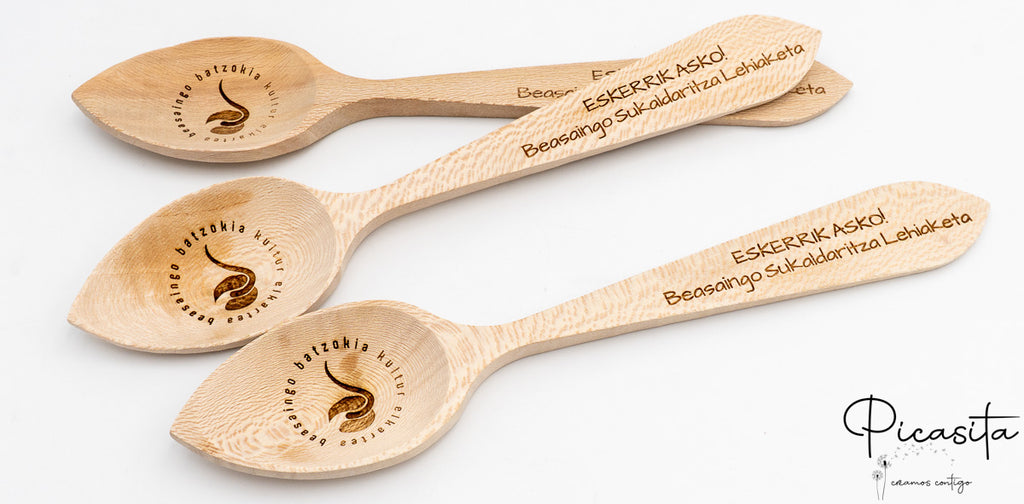 Tres cucharas de madera grabadas con mensajes de agradecimiento y logotipos de concursos culinarios.