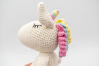 Perfil de la cabeza de un unicornio de crochet blanco mostrando el cuerno y melena espiral.