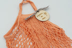 Detalle de bolsa naranja con placa de madera personalizada y lazo de cuadros marrones.