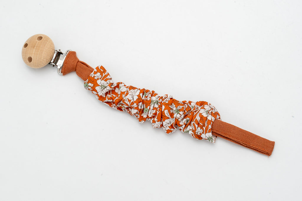 Gerafftes Schnullerband mit Blumen auf terrakottafarbenem Hintergrund und Holzclip