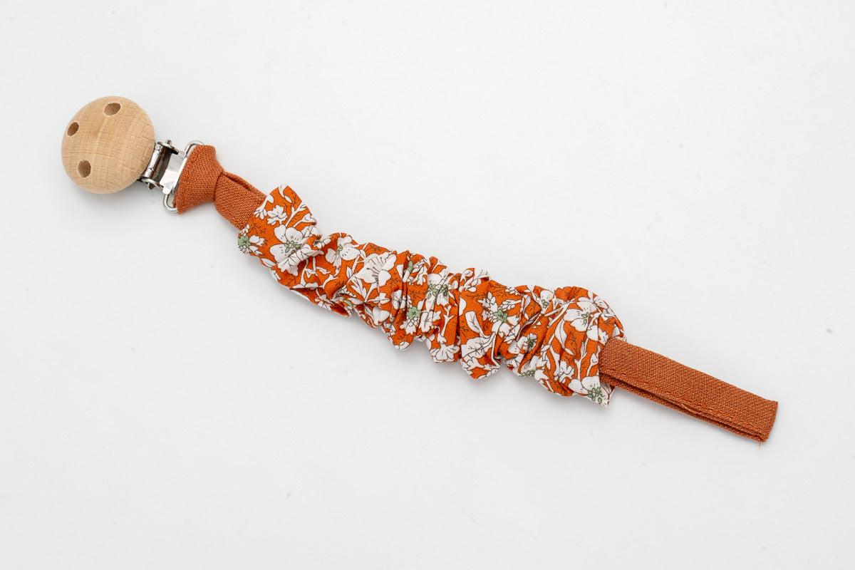 Gerafftes Schnullerband mit Blumen auf terrakottafarbenem Hintergrund und Holzclip