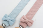 Detail der Schnullerbänder mit hellblauer und rosa Schleife neben den Holzclips