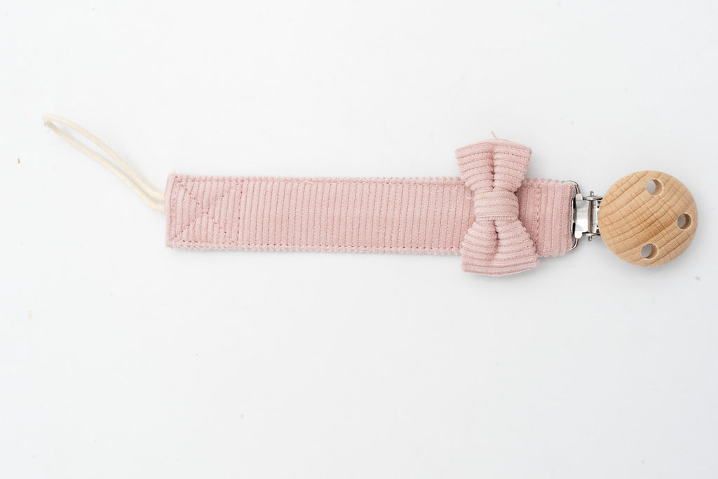 Rosa Schnullerband mit Schleife neben dem runden Holzclip