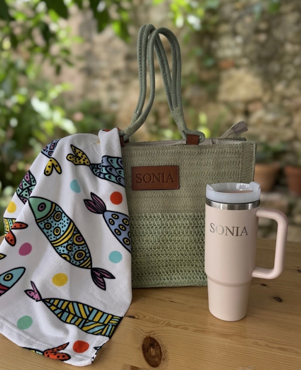 Bolso de rafia verde con nombre Sonia grabado y toalla blanca con estampado de peces.