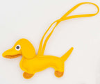 Accesorio de polipiel amarilla con forma de perro salchicha y tira larga de sujeción.
