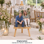 Lienzo de 15 × 20 cm con foto preboda de Emma y Oliver y el texto «Table 7», sobre caballete en una mesa de banquete.