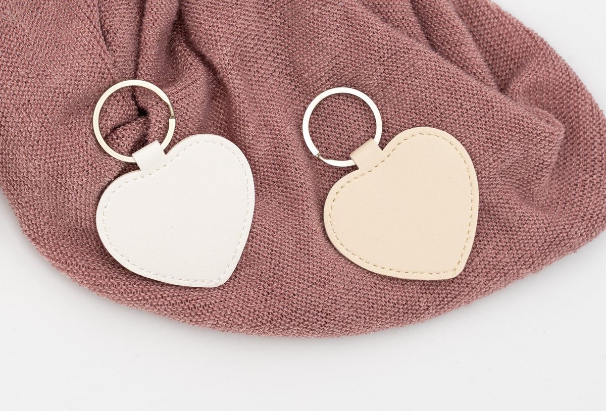 Weiße und beige Herz-Schlüsselanhänger ohne Personalisierung auf rosa Stoff.