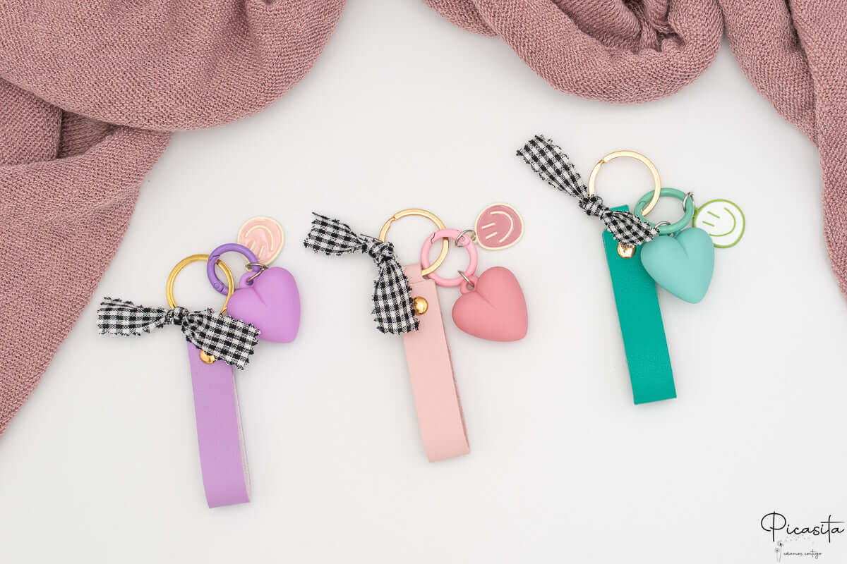 Tres llaveros personalizados en colores púrpura, rosa y aguamarina con charms y anillas doradas.