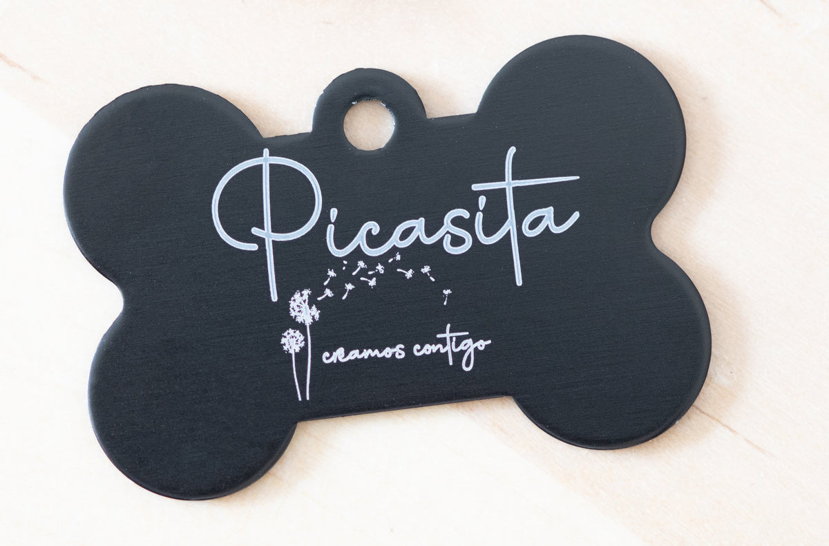 Placa de identificación negra en forma de hueso con grabado láser blanco de nombre y diseño floral.