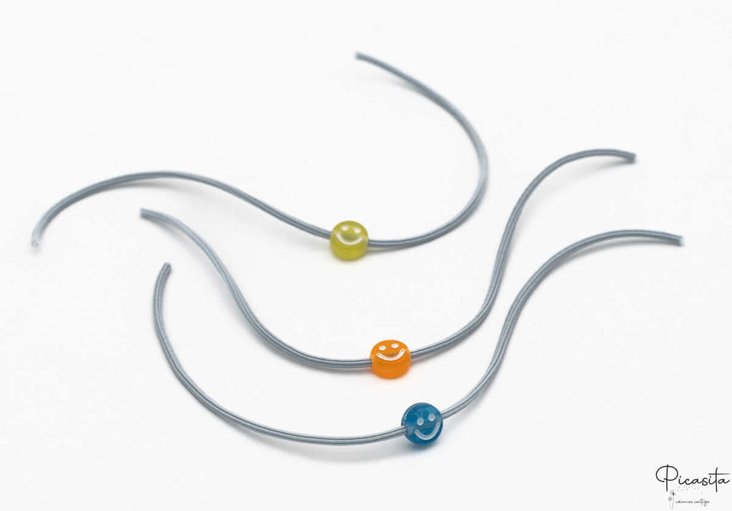 Detalle de pulseras infantiles con cuentas de silicona de caritas sonrientes sobre cordón elástico gris.
