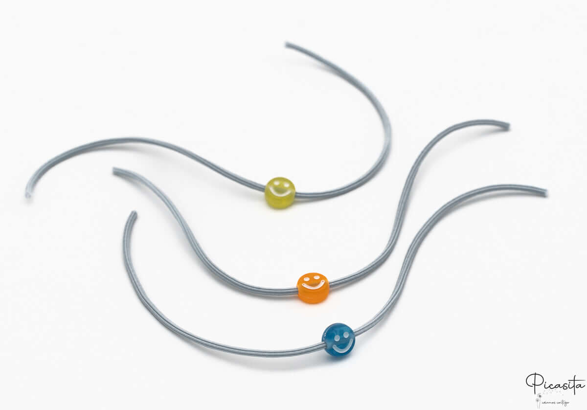Detalle de pulseras infantiles con cuentas de silicona de caritas sonrientes sobre cordón elástico gris.