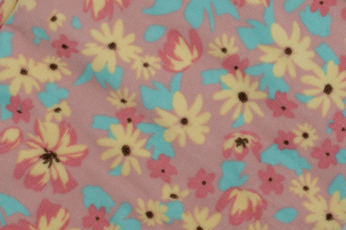 Detalle de tejido de toalla rosa con estampado floral de margaritas amarillas y azules.