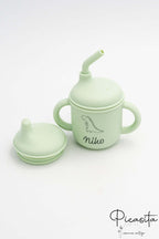 Vaso infantil verde clarito de silicona con pajita y tapa de boquilla adicional.
